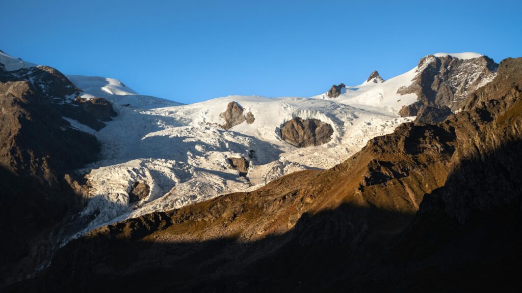 Breathtaking view of a snow-covered Alpine glacier illuminated by warm sunset light.
