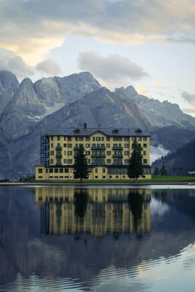 Charming lakeside hotel reflecting in calm water with majestic mountain backdrop.
